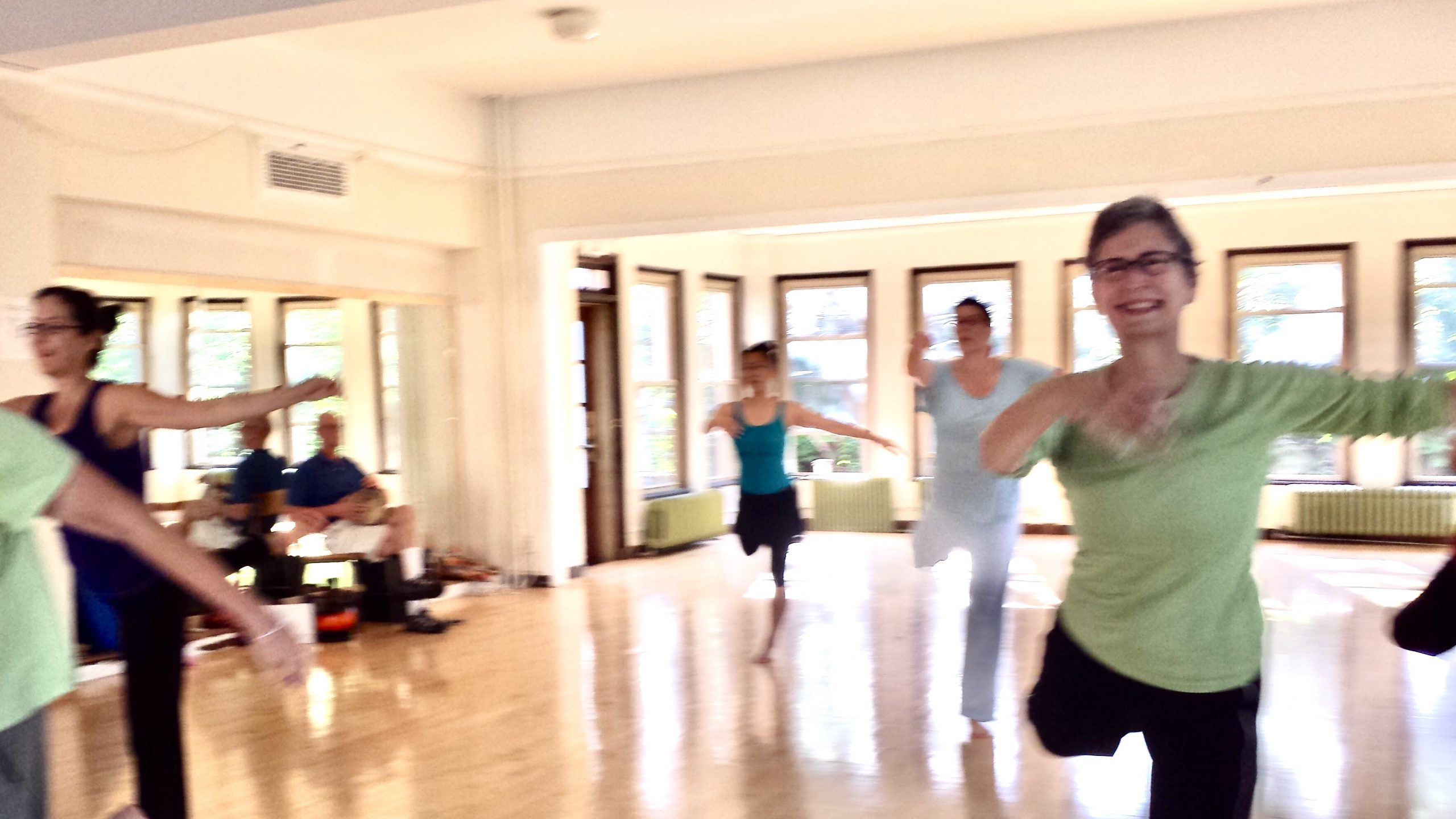 A group of dancers jump on one leg in a large studio