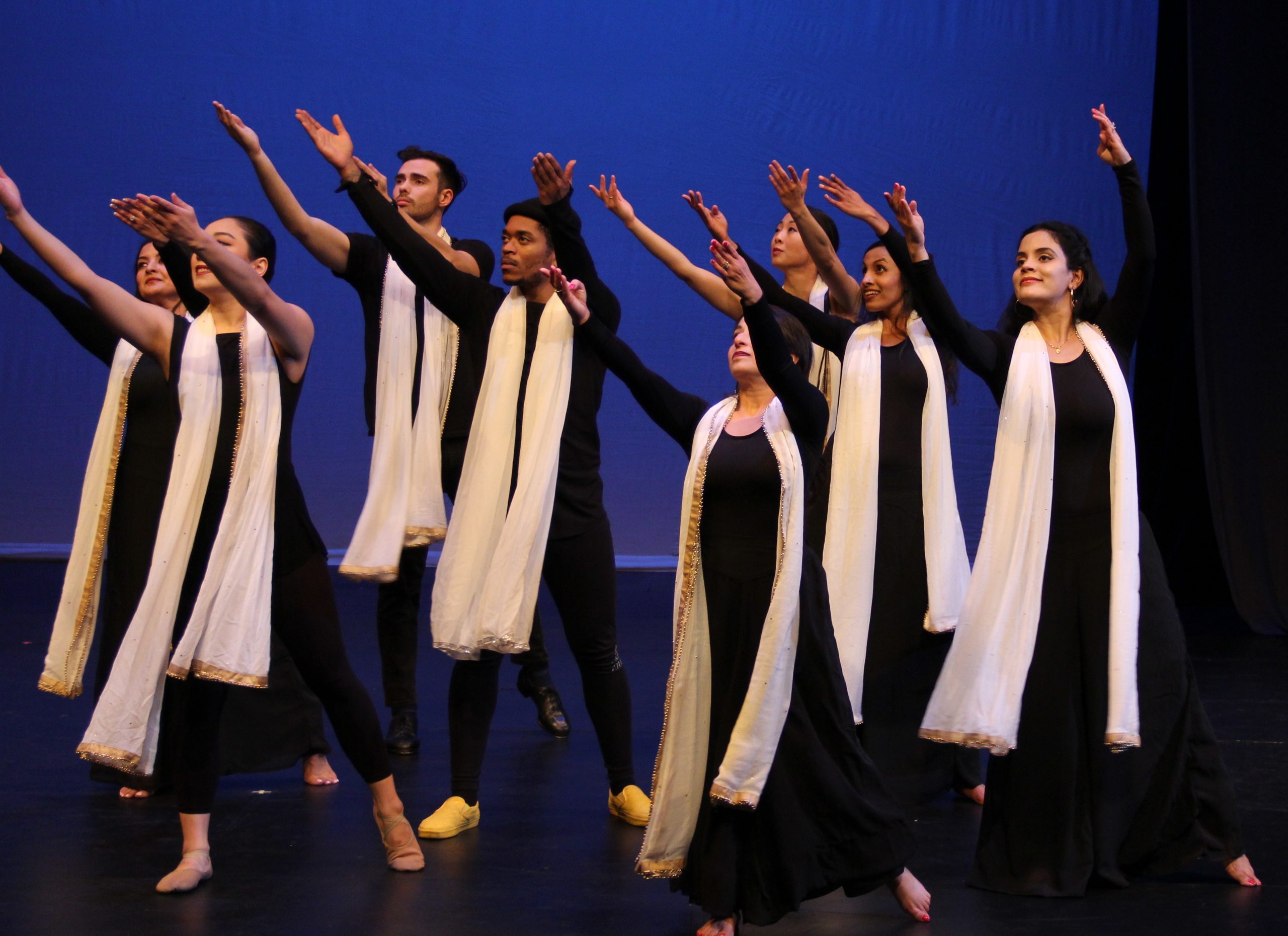 The dancers of Katha Dance Theatre stand on stage and gesture with their right arms pointing off to the right