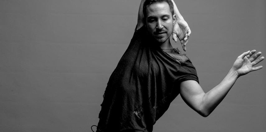 a light-skinned man wraps his right arm behind his head and lifts his left hand up